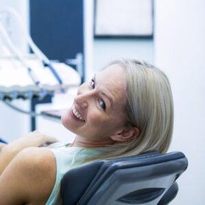 A blonde woman in a dentist's chair looks back to smile at the camera with straight white teeth
